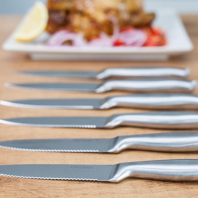 Cuchillos Cecotec de carne colocados sobre mesa junto a plato de comida