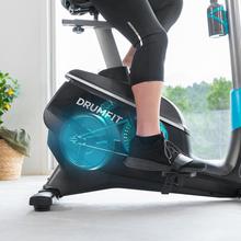 Vélo d'appartement DrumFit Cycle 9000 Talos Pro. Résistance magnétique réglable avec moteur, guidon avec capteur de fréquence cardiaque, selle réglable, support pour dispositifs et roues.