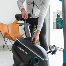 Vélo d'appartement DrumFit Cycle 9000 Talos Pro. Résistance magnétique réglable avec moteur, guidon avec capteur de fréquence cardiaque, selle réglable, support pour dispositifs et roues.