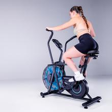 Drumfit WOD Rider 2000 Eolo PRO es una bicicleta de aire para entrenamientos intensivos, con ventilador de 480 mm y resistencia progresiva, pedaleo silencioso por correa, pantalla LCD, medidor de pulso en las asas, ruedas de transporte, compatibilidad y capacidad máxima de 135 kg.